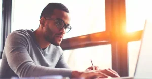 young man with glasses works diligently in front of laptop