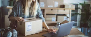 young woman working in front of laptop with shipping labels and boxes