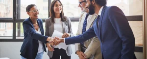 four smiling business people shaking hands and holding papers