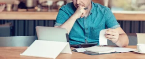 middle-aged man works in front of tablet with calculator and notebook in coffee shop