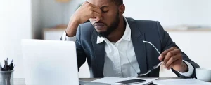 frustrated businessman pinches bridge of nose in front of laptop