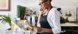 young female worker talks on phone in front of register in coffee shop