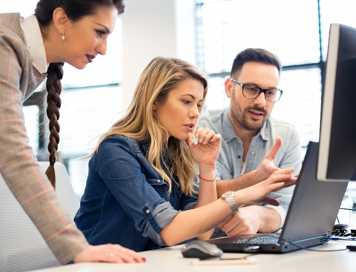 group of three smiling businesspeople reviewing content on laptop screen